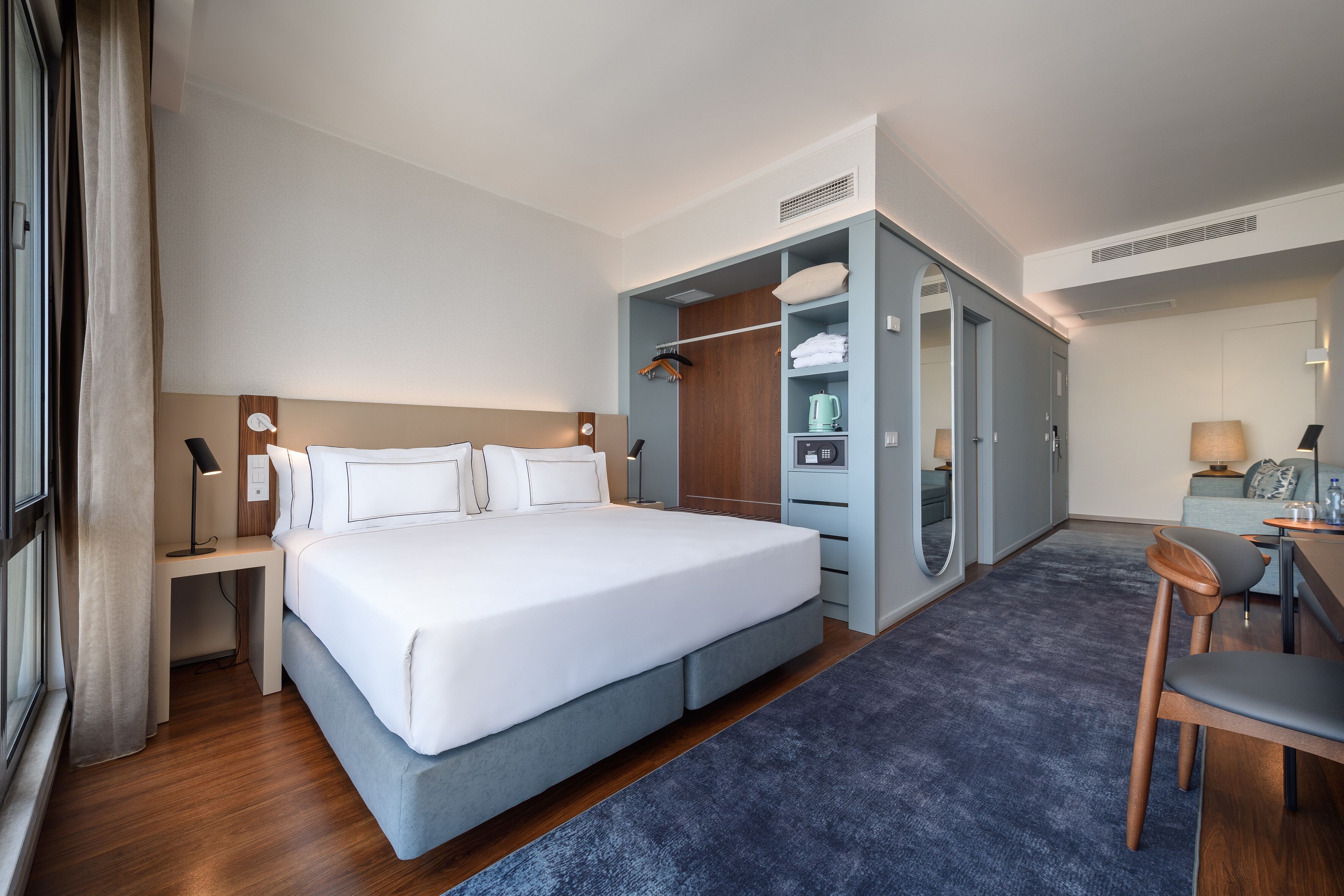 Una habitación de hotel moderna con una cama grande, un escritorio, una silla, un armario y un baño.