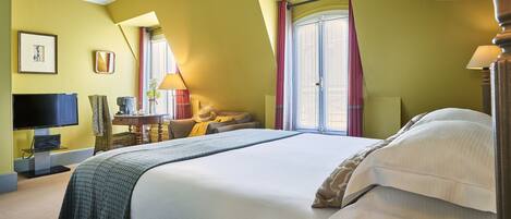 Una habitación de hotel con una cama grande, televisión, escritorio con lámpara y ventana con cortinas.
