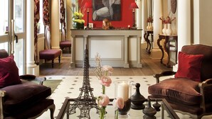 A lobby with a fireplace, red walls, and a large painting. There are two armchairs and a table with a candle and flowers.