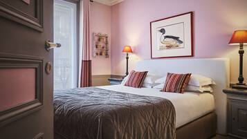 A bedroom with a bed, two bedside tables, a nightstand, a framed picture on the wall, and a window with curtains.