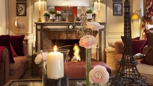 A cozy living room with a fireplace, a glass table with a candle, and decorative flowers.