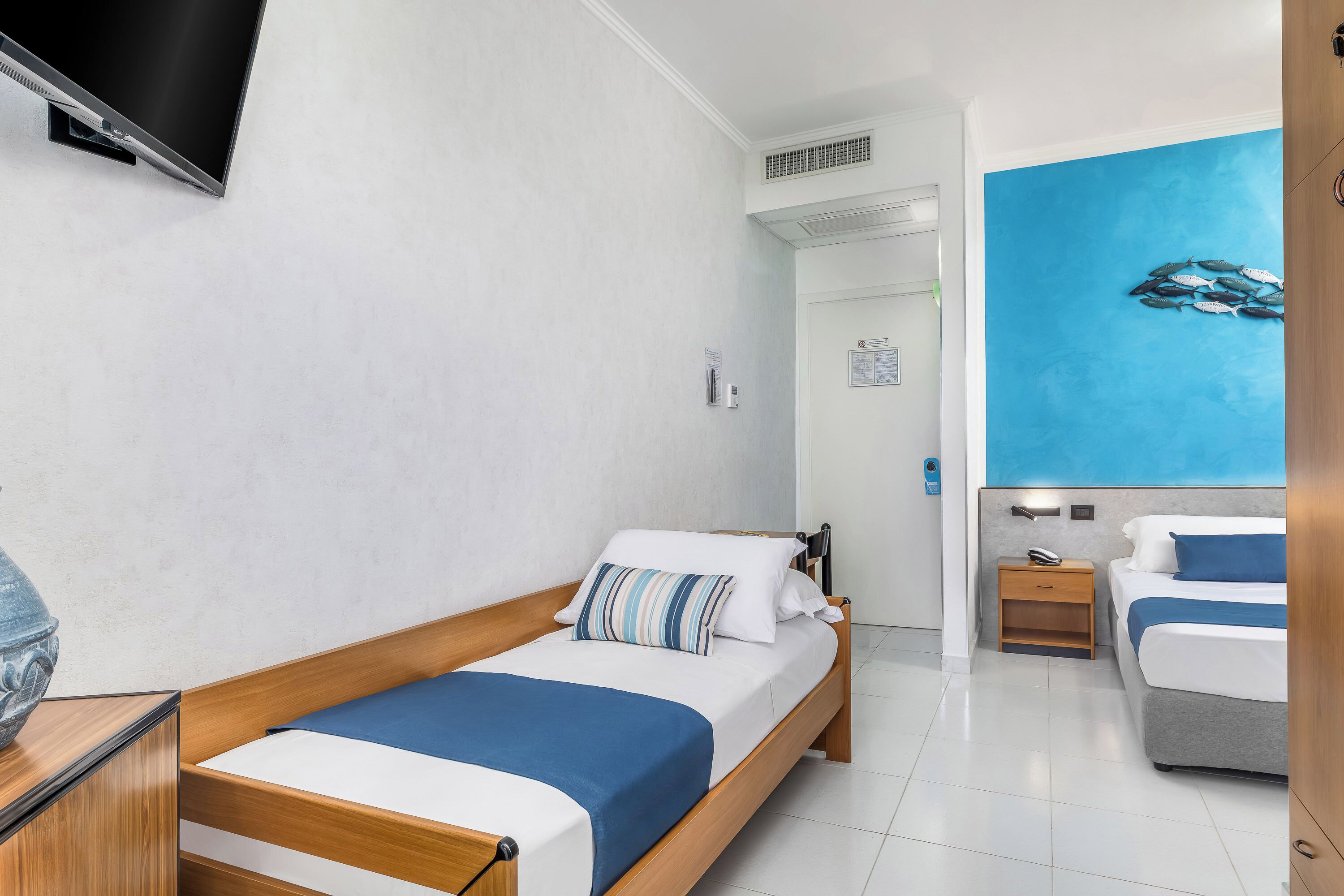 Una camera d'albergo moderna con un letto di legno, una TV, un affresco blu e un letto separato nella stanza adiacente.