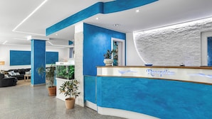 A reception area with a blue and white color scheme, a reception desk, potted plants, and a seating area with a sofa and a coffee table. - Hotel Blu Eden - Calabria oltre il Mare - Adults Only (Praia a Mare)