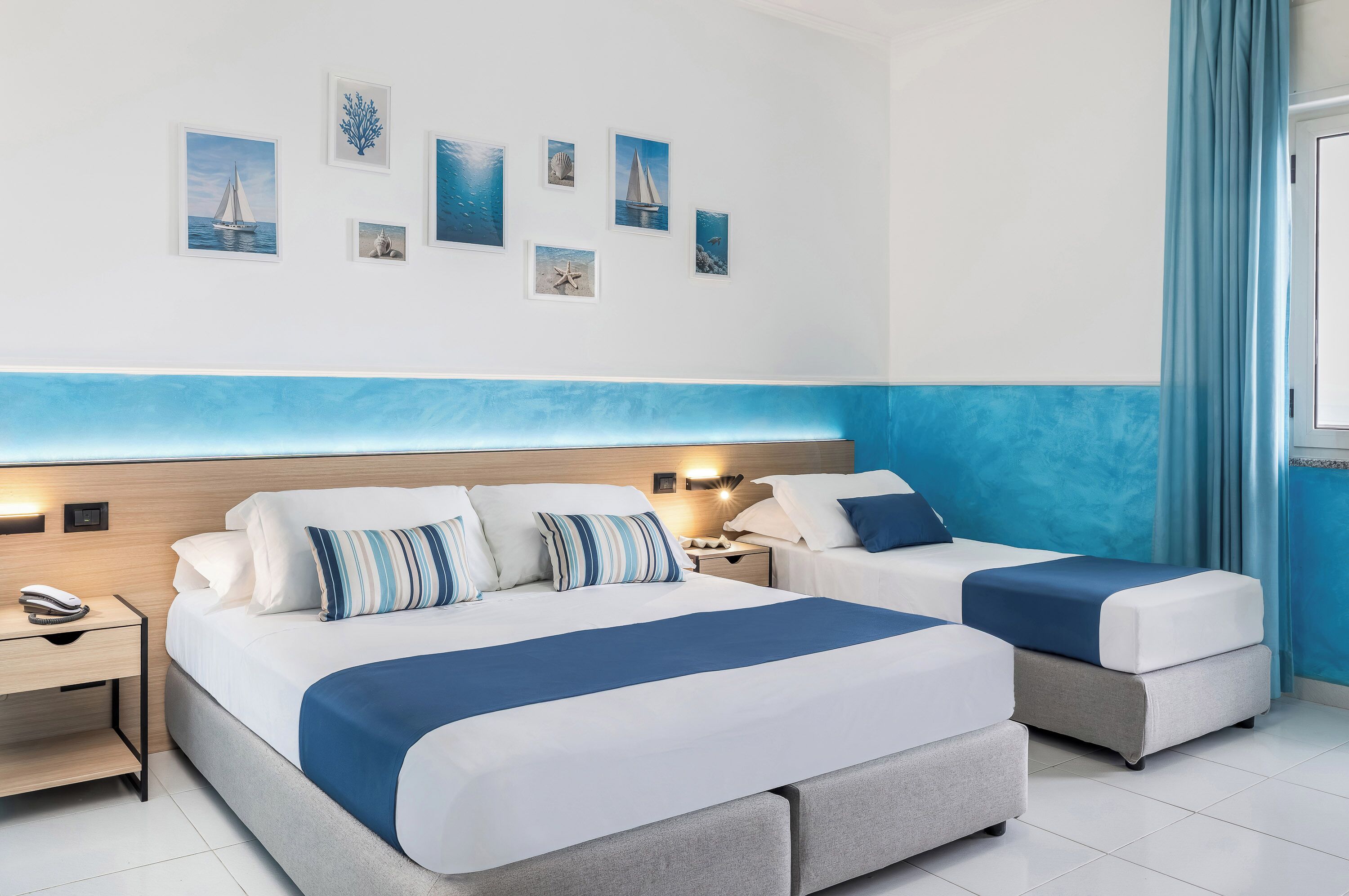 Une chambre d’hôtel avec deux lits, un mur d’accent bleu et des œuvres d’art murales sur le thème de la marine.