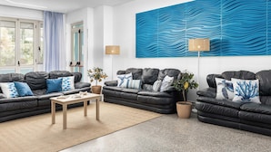 A modern living room with black leather sofas, a wooden coffee table, and a large blue abstract wall art piece. - Hotel Blu Eden - Calabria oltre il Mare - Adults Only (Praia a Mare)