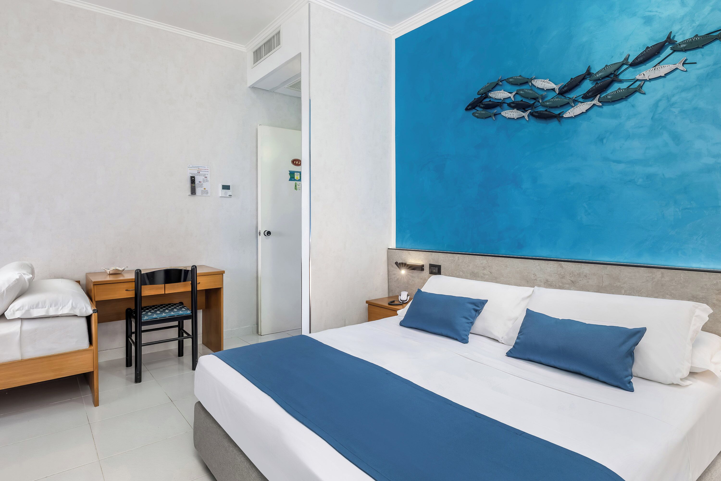 A hotel room with a bed, a desk, a chair, and a wall painting.