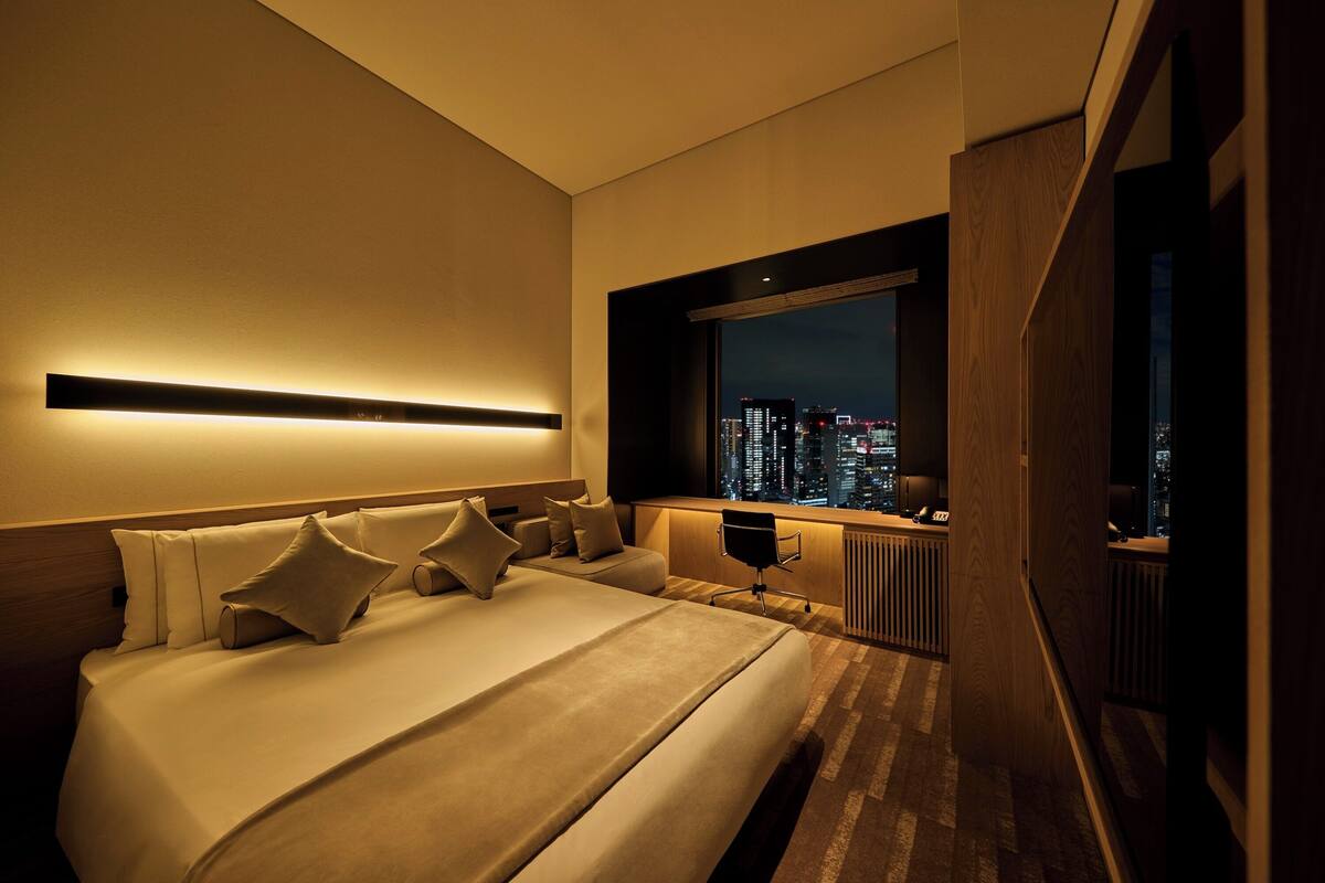 Een moderne hotelkamer met een groot bed, uitzicht op de stad en een bureau met stoel.