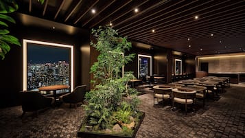 A modern lounge with a city view, a central indoor plant, and multiple seating areas.