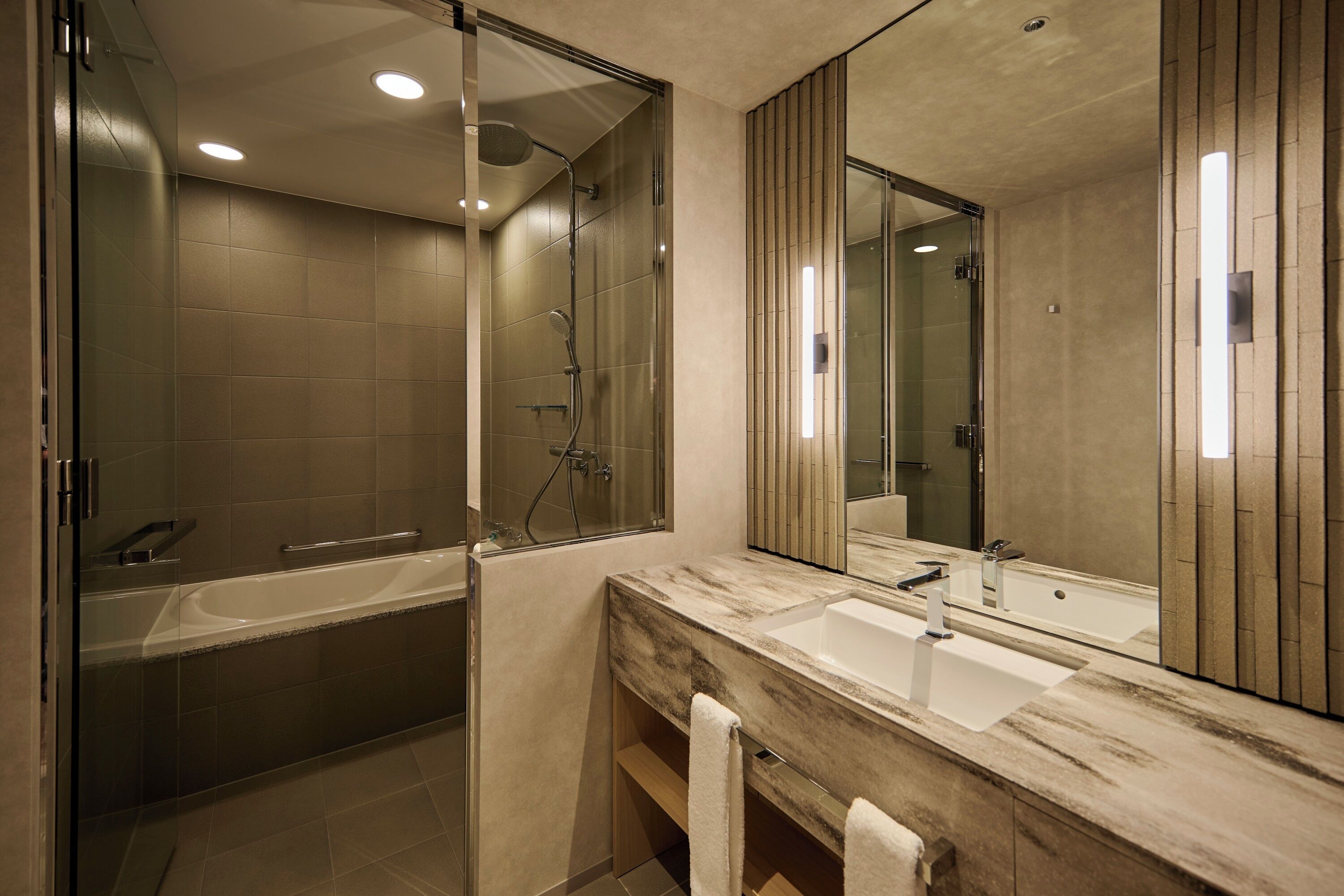 A modern bathroom with a large mirror, two sinks, a bathtub, and a shower.