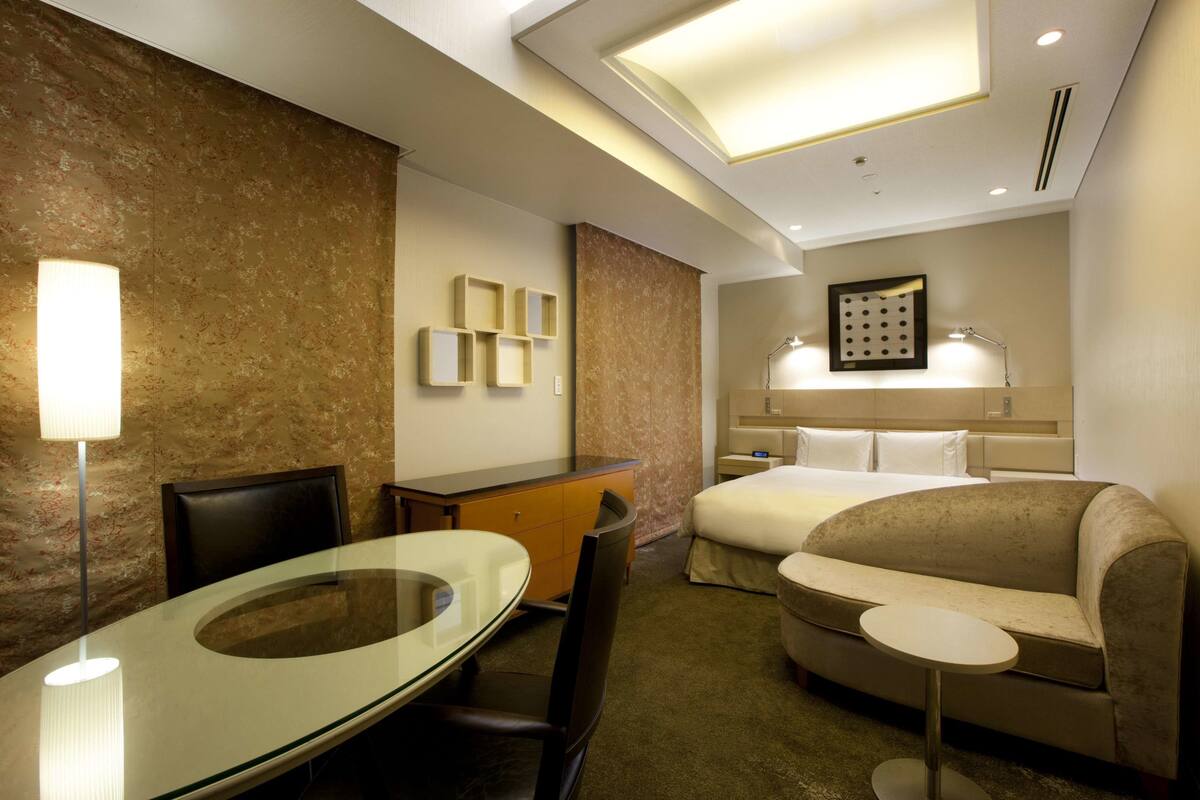 Een hotelkamer met een glazen tafel, een bank, een bed, een bureau en een lamp.