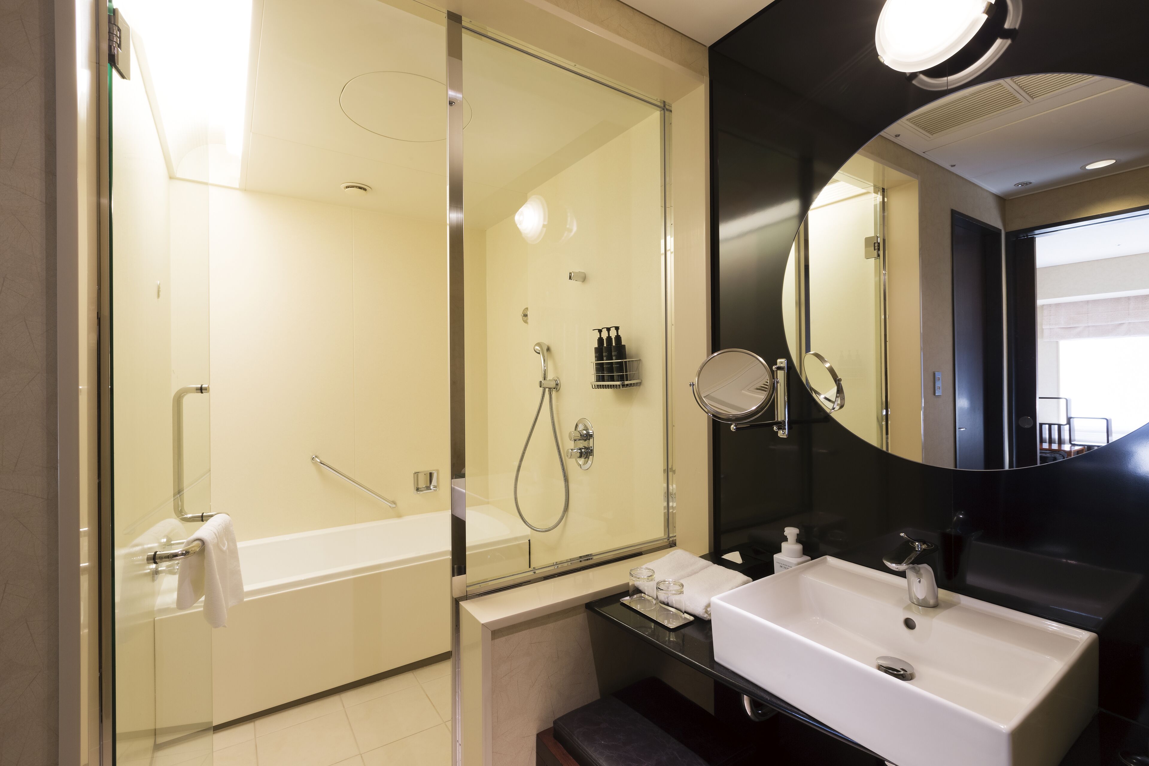 A modern bathroom with a glass-enclosed shower, a white sink, and a large mirror.