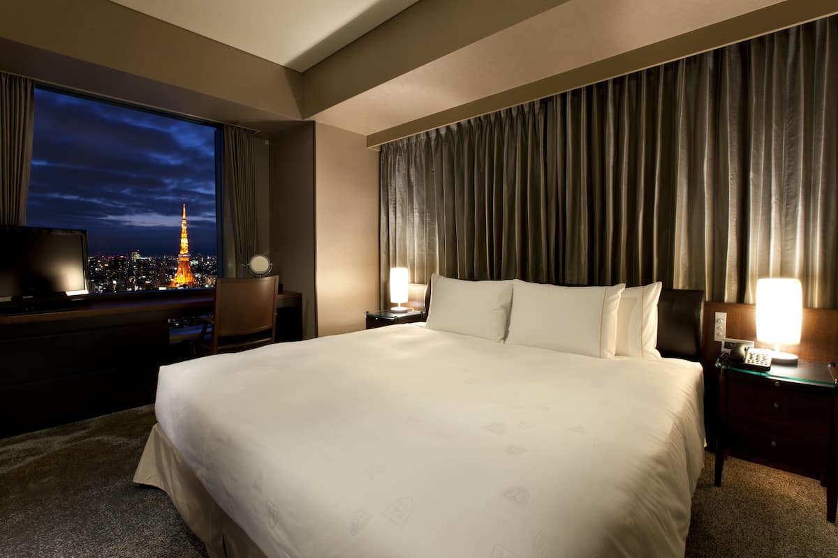Hotelkamer met een groot bed, een televisie aan de linkerkant en uitzicht op een stadsbeeld met een toren.