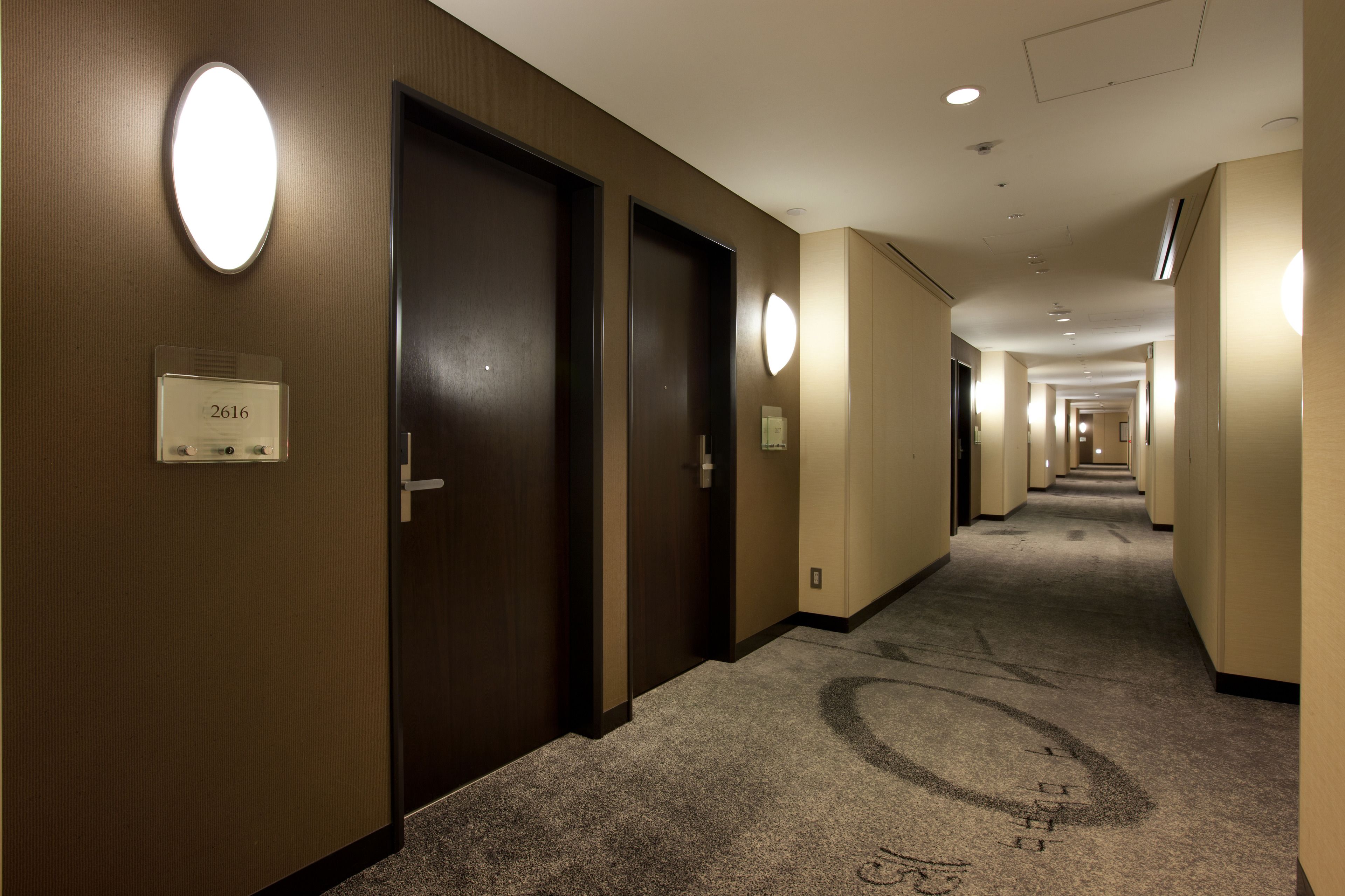 A hotel hallway with dark wooden doors, numbered room signs, and a carpeted floor.