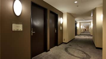 A hotel hallway with dark wooden doors, numbered room signs, and a carpeted floor.