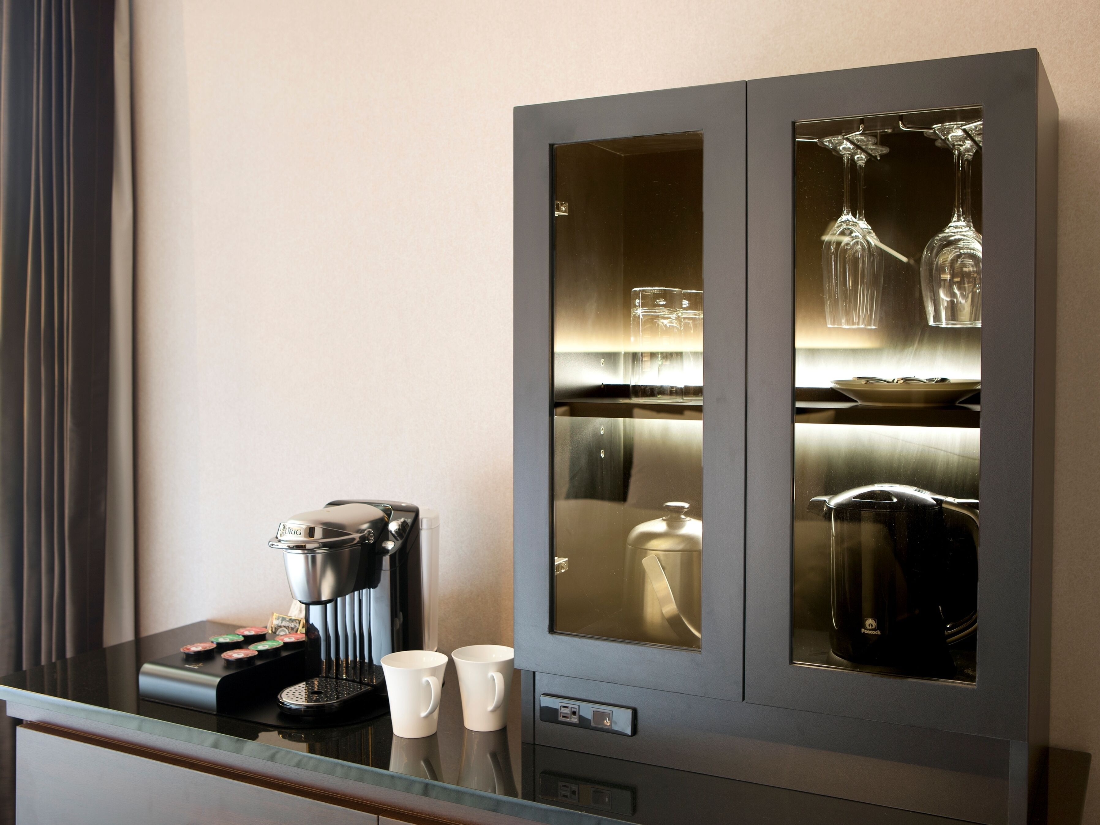 A minibar with a coffee maker, two cups, and a glass of water.