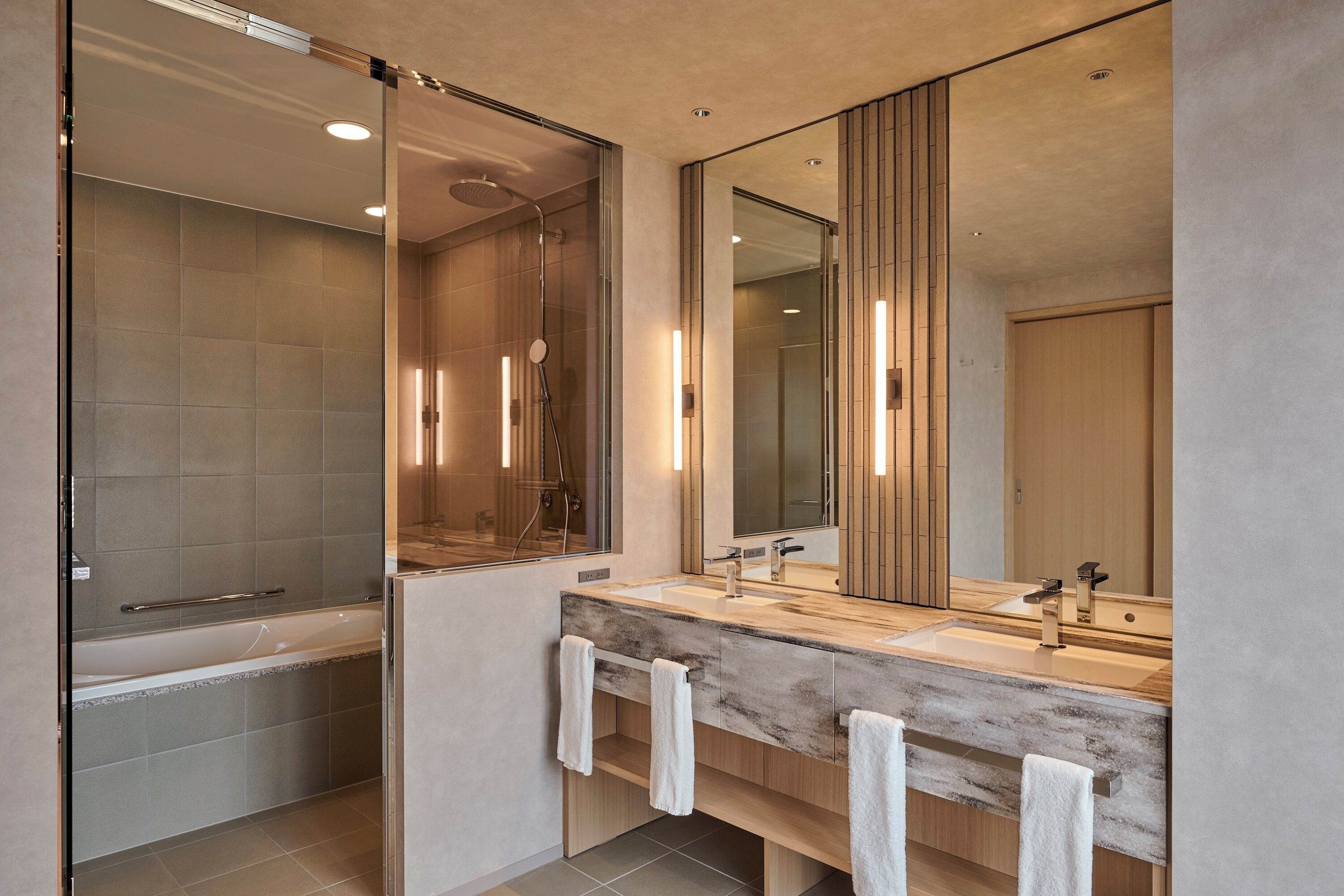Een moderne badkamer met een douchecabine van glas, een grote spiegel en een houten wastafelmeubel met twee wasbakken.