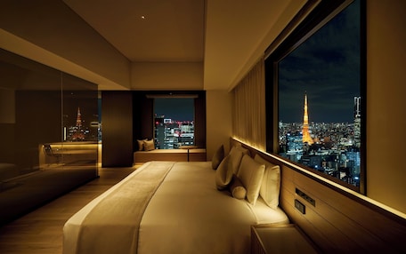 A modern hotel room with a large bed, a seating area, and a city view.