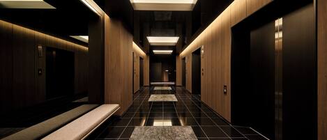 A modern elevator lobby with a long corridor, wooden paneling, and a bench.