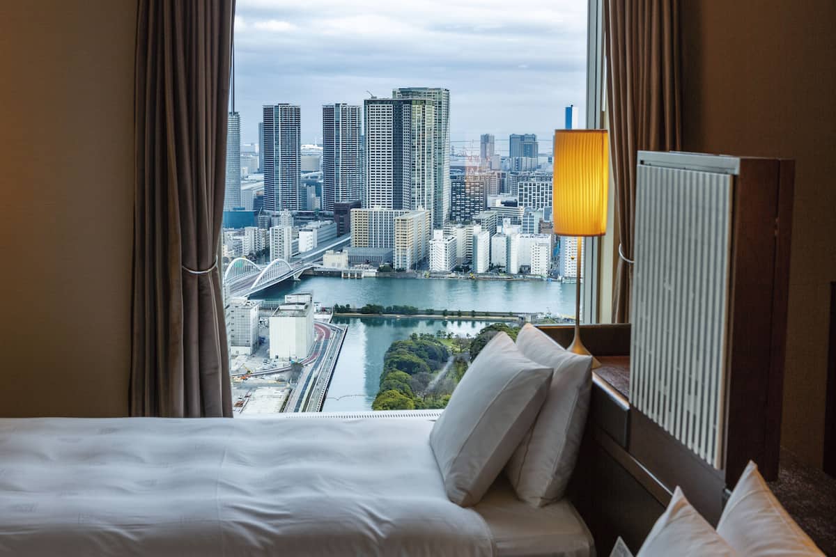 Een hotelkamer met een bed, uitzicht op een stadsbeeld en een lamp.
