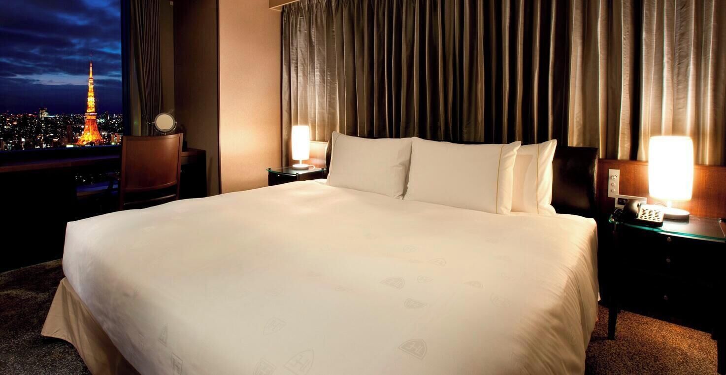 Hotelkamer met een groot bed, twee nachtkastjes met lampen en uitzicht op de Eiffeltoren, met een gordijnen als achtergrond.