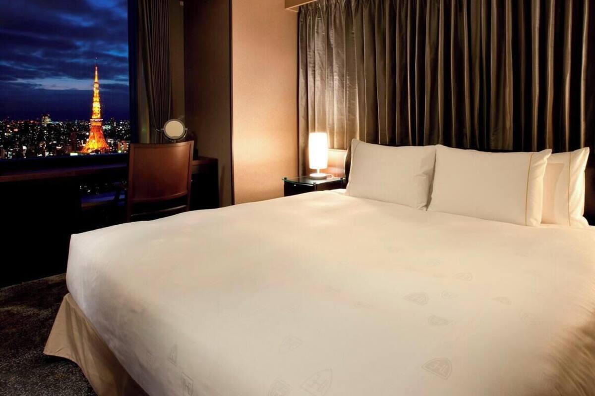Hotelkamer met een groot bed, twee nachtkastjes met lampen en uitzicht op de Eiffeltoren, met een gordijnen als achtergrond.