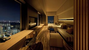 Een moderne hotelkamer met uitzicht over de stad, een bureau met telefoon, een bank en een bed.