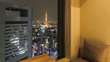 A room with a large window overlooking a cityscape at night, featuring illuminated buildings and a prominent tower.