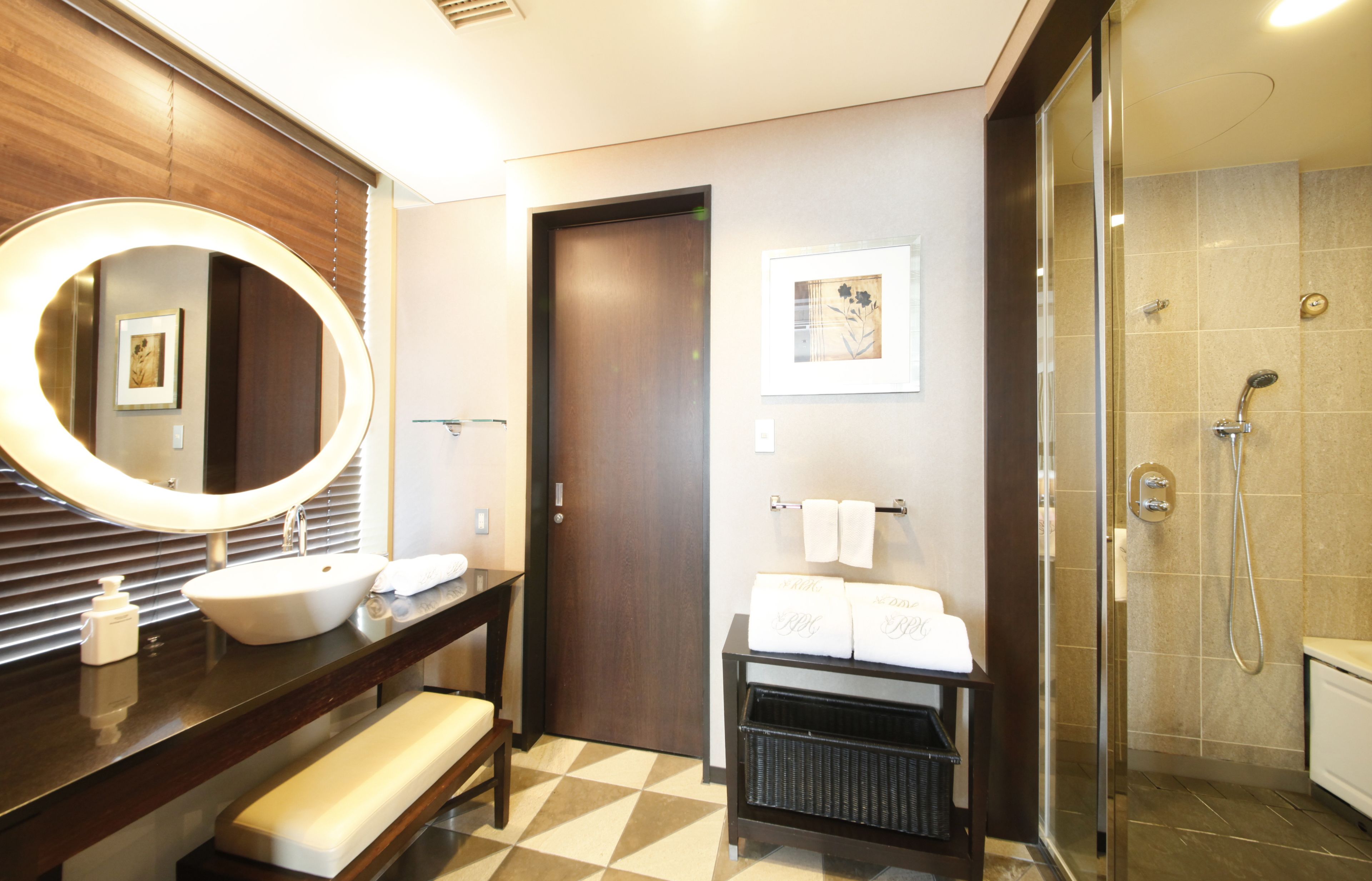 A modern bathroom with a large mirror, a sink, a bench, a towel rack, and a shower area.