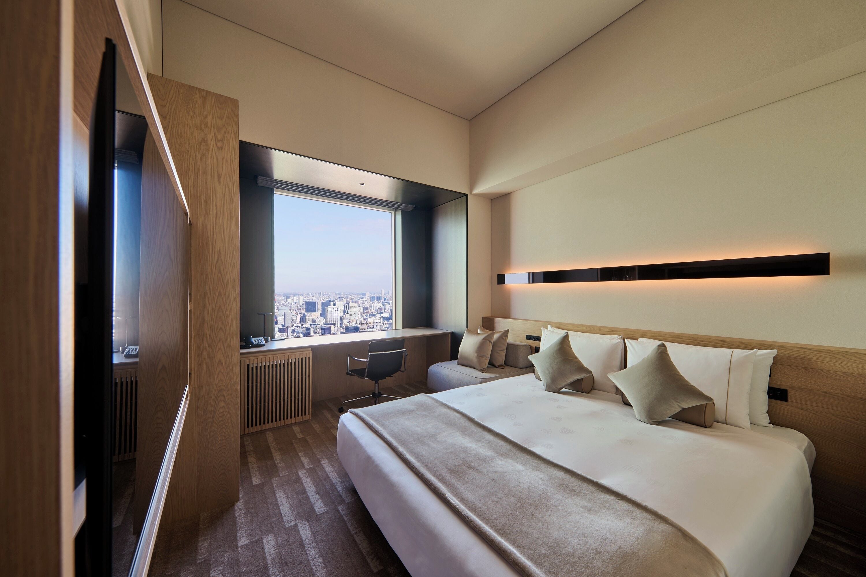 A modern hotel room with a large bed, a desk, and a view of the city.