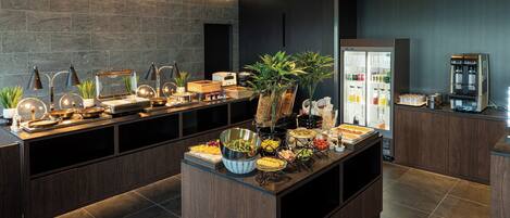 A modern kitchen with a buffet setup, including a variety of food items and a coffee machine.