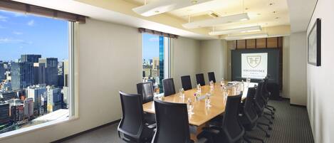 A conference room with a city view, a long table with chairs, and a presentation screen.