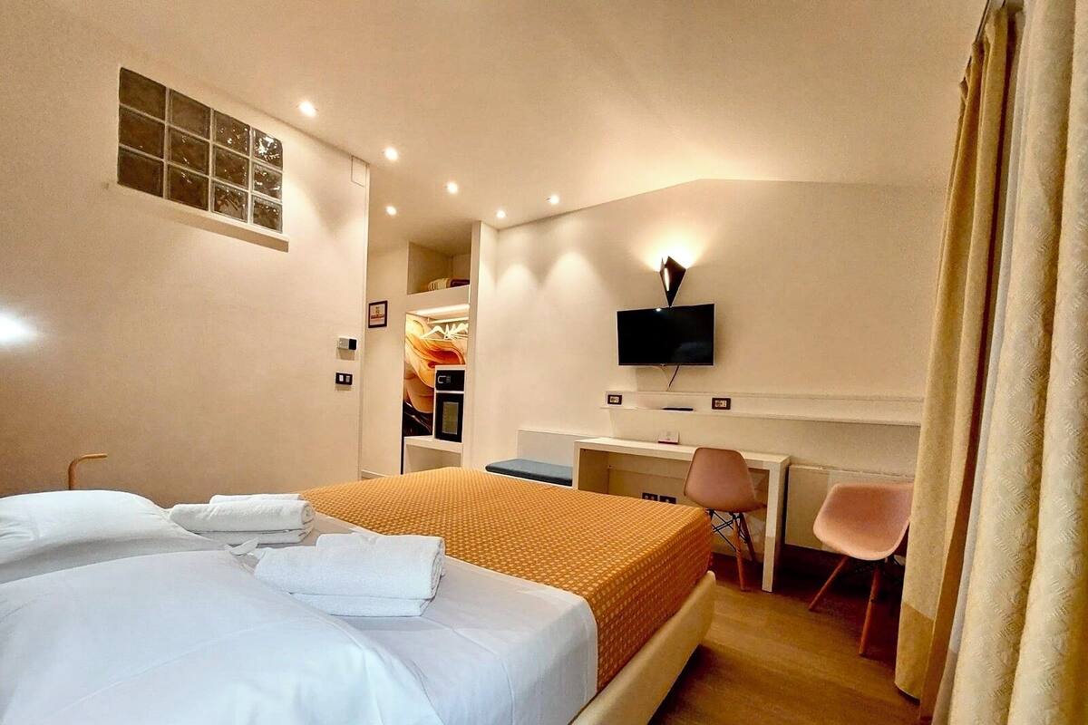 A hotel room with a bed, a desk, a chair, a television, and a window.