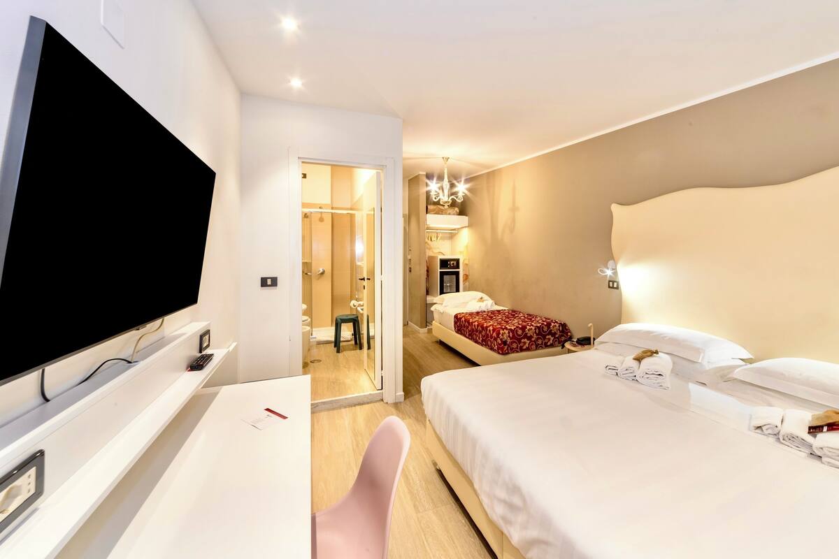A hotel room with a large bed, a TV, a desk, and a shower area.