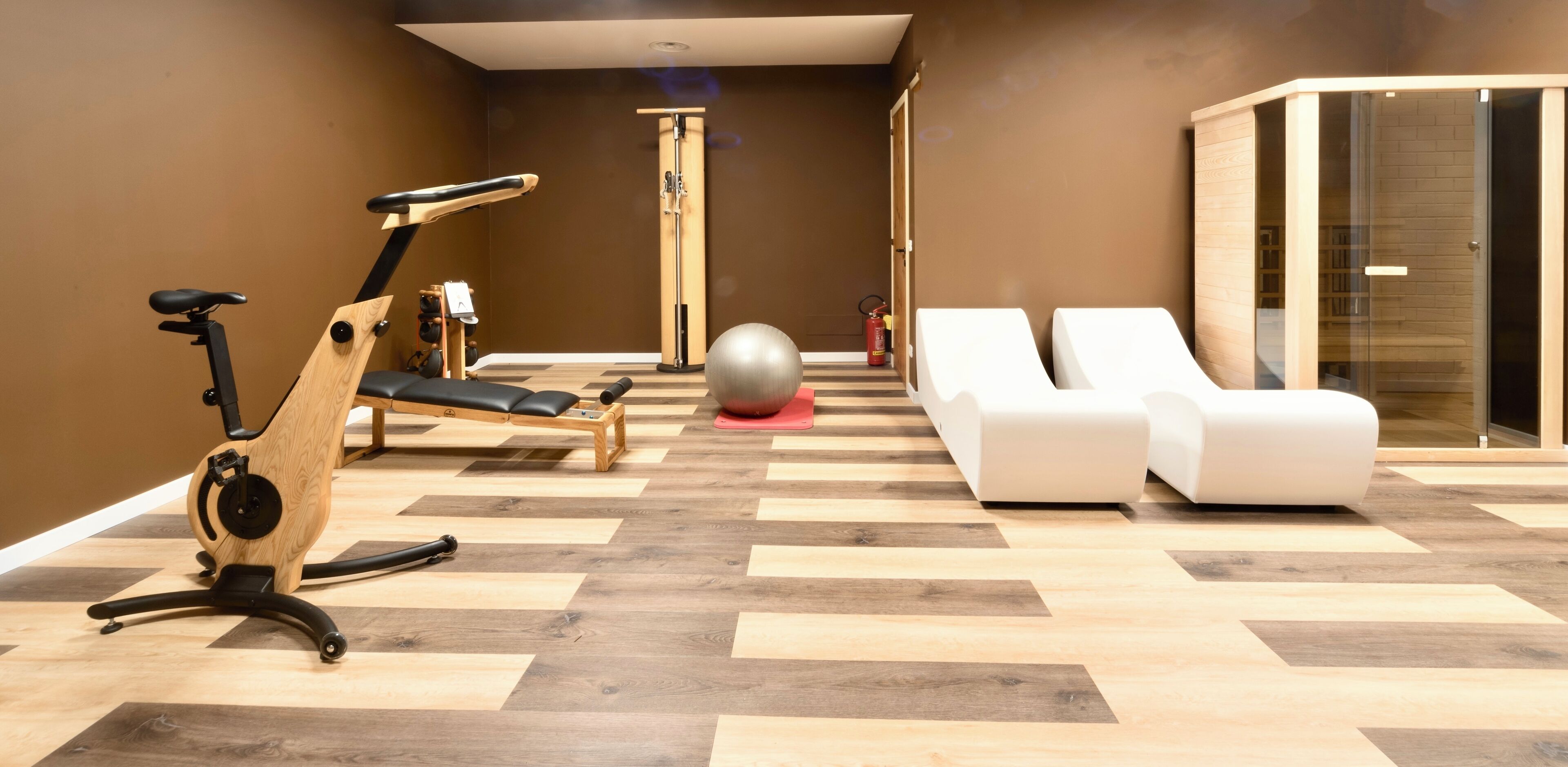 Ein modernes Fitnessstudio mit Trainingsgeräten, einem Massagesessel und einem Entspannungsbereich mit zwei Liegestühlen.
