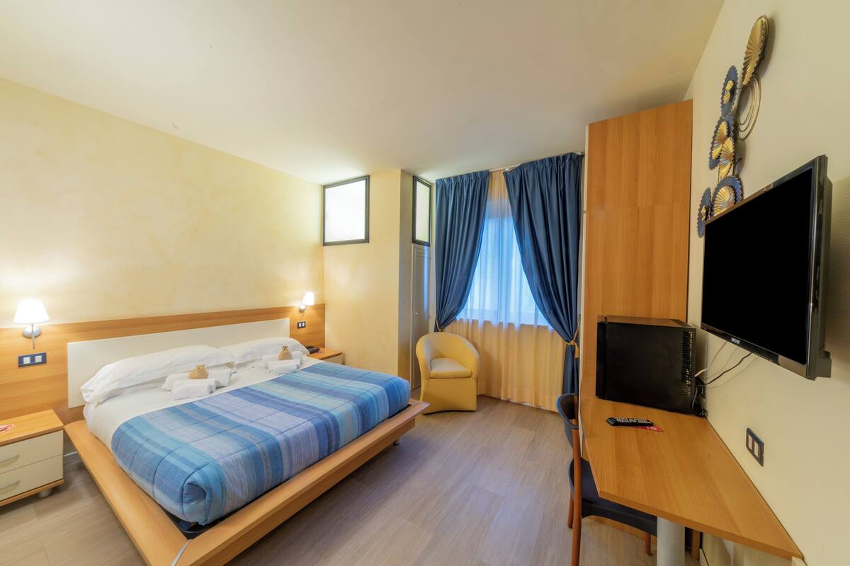 A hotel room with a bed, a desk, a TV, and a chair.