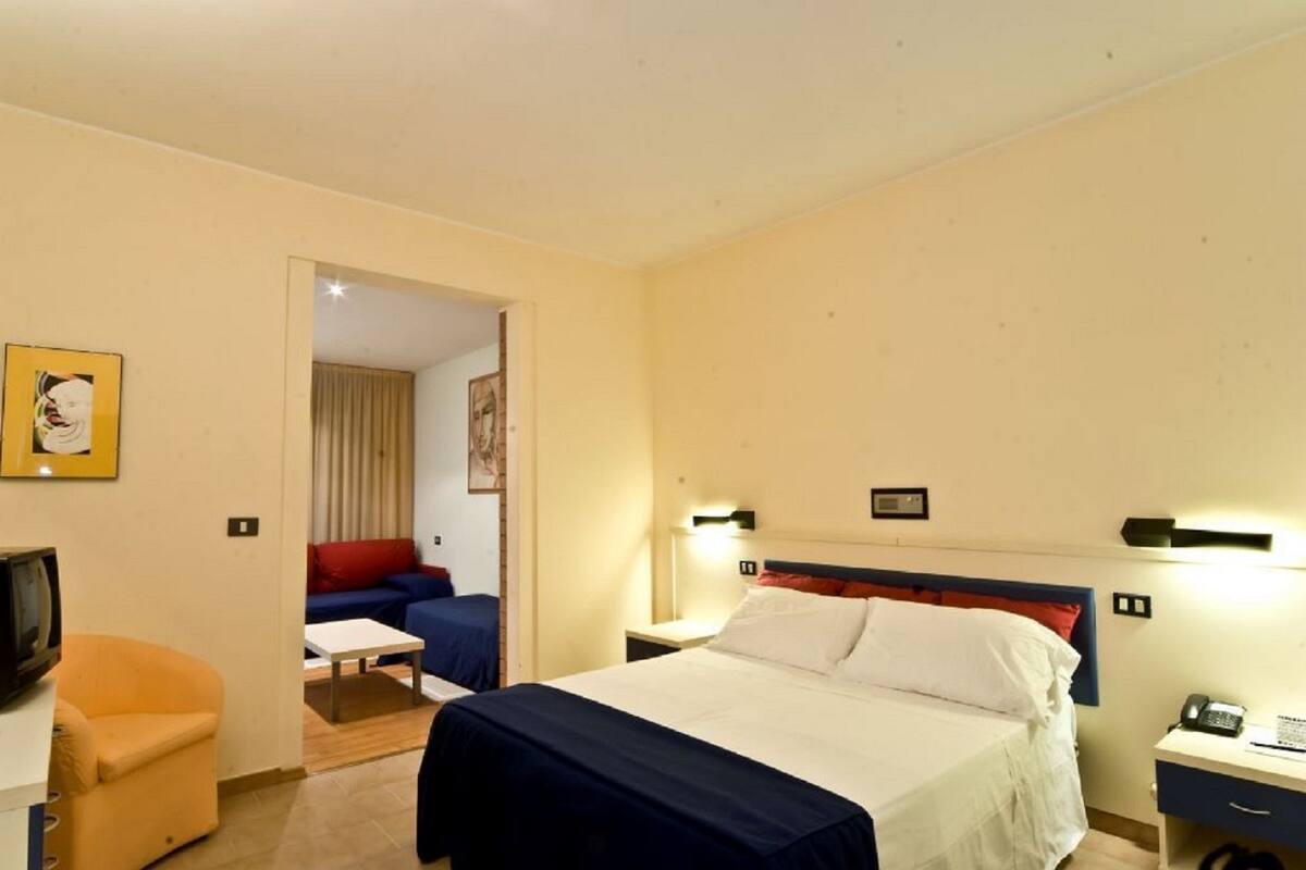 A hotel room with a bed, a desk, a chair, a television, and a sofa.