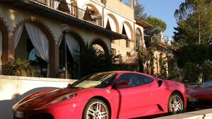 A red sports car parked in front of a building with arched windows and balconies. - Hotel El Patio (Corciano)