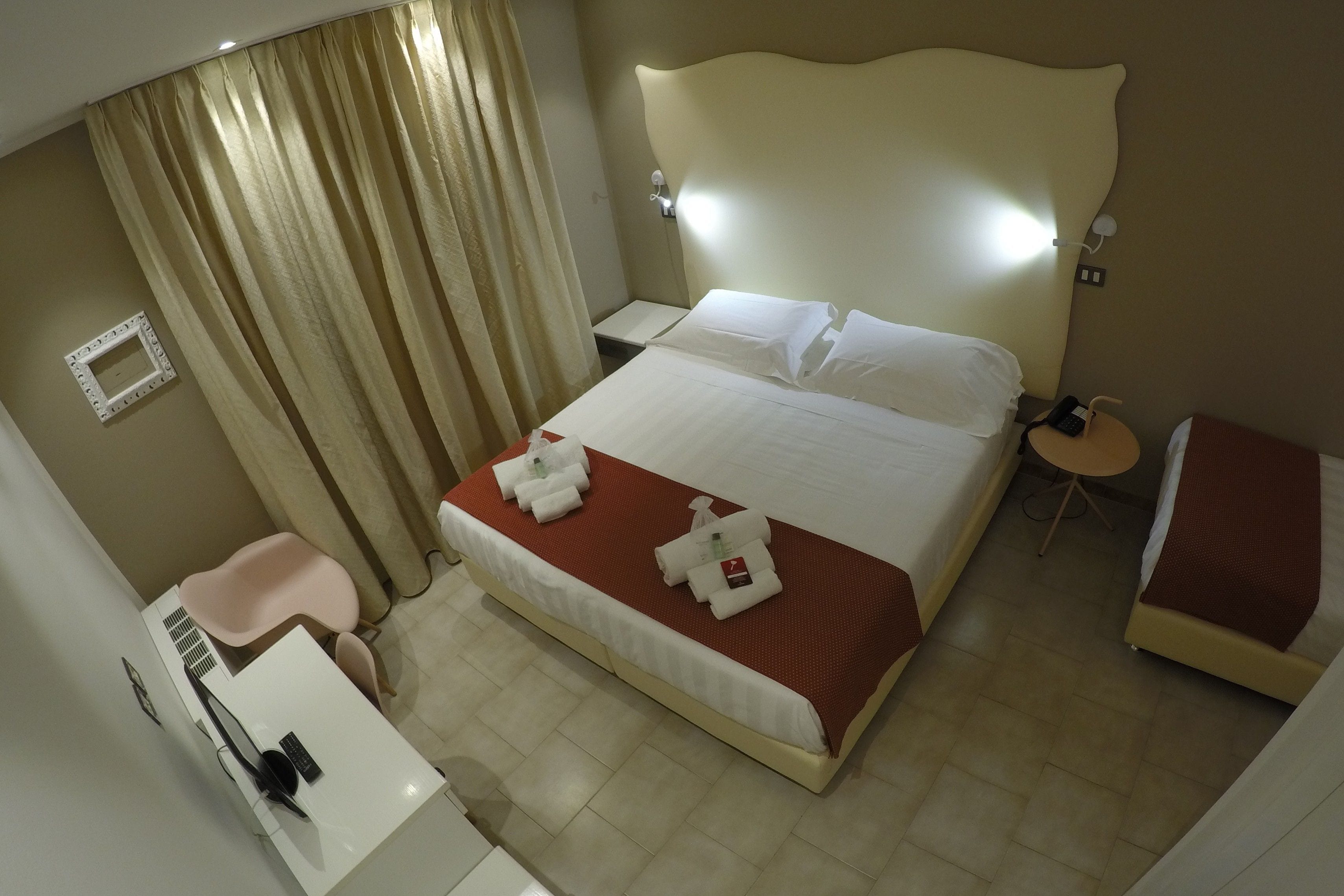 A hotel room with a bed, bedside table, chair, and a small desk with a chair.