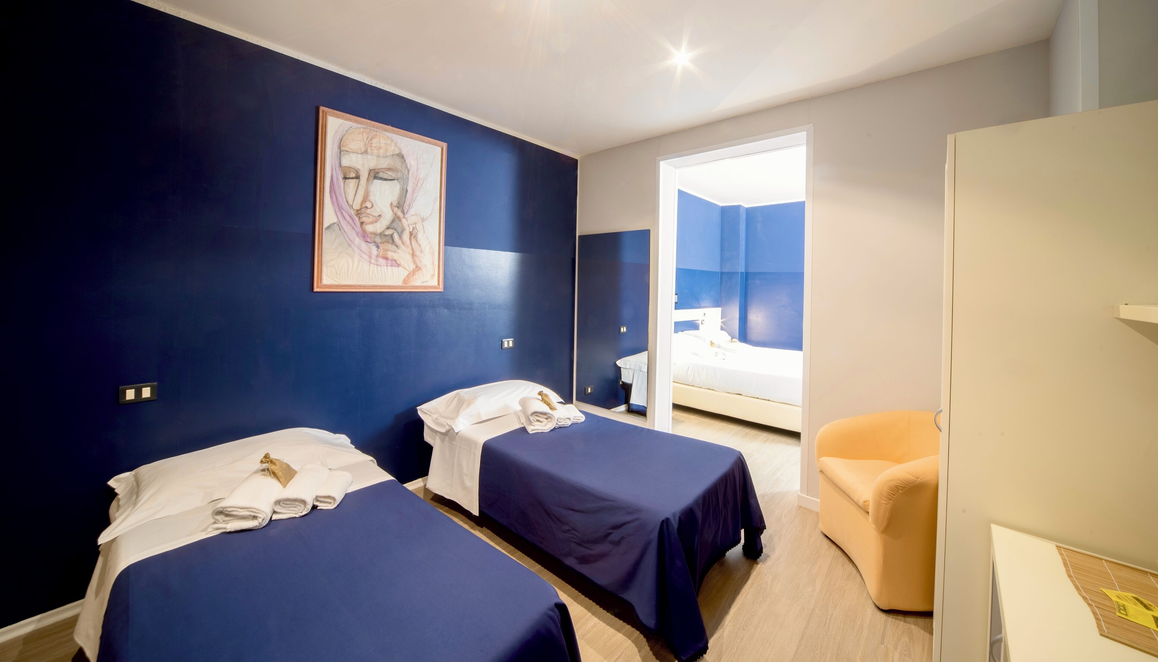 Ein Hotelzimmer mit zwei Betten, einem Bild an der Wand, einem Sessel und einem durchgegangenen Tür erkennbaren Badezimmer.