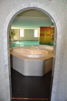 Uma área de spa com uma banheira grande e uma banheira menor, piso revestido e parede com padrão hexagonal.