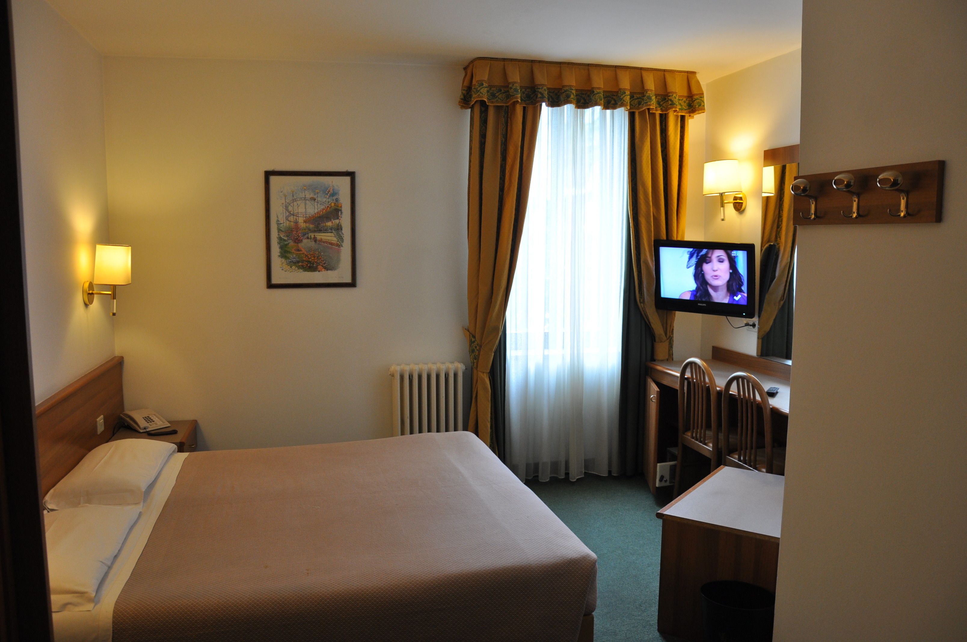 Una habitación de hotel con cama, lámpara de noche, televisor, escritorio y silla.