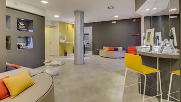A modern hotel lobby with a curved sofa, a yellow chair, and a reception desk with a computer.