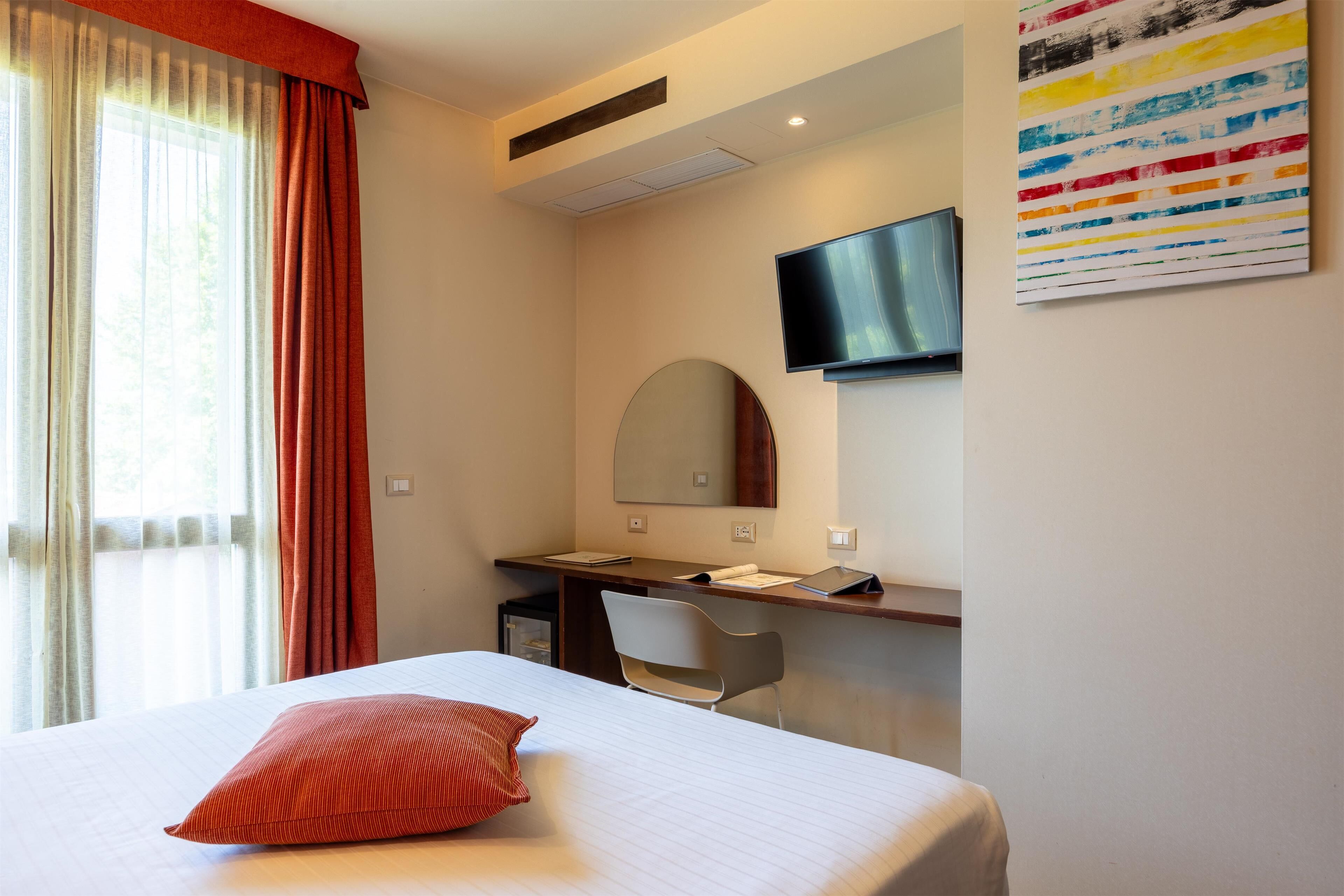 Una habitación de hotel con cama, escritorio, silla, televisor y una obra de arte colorida en la pared.