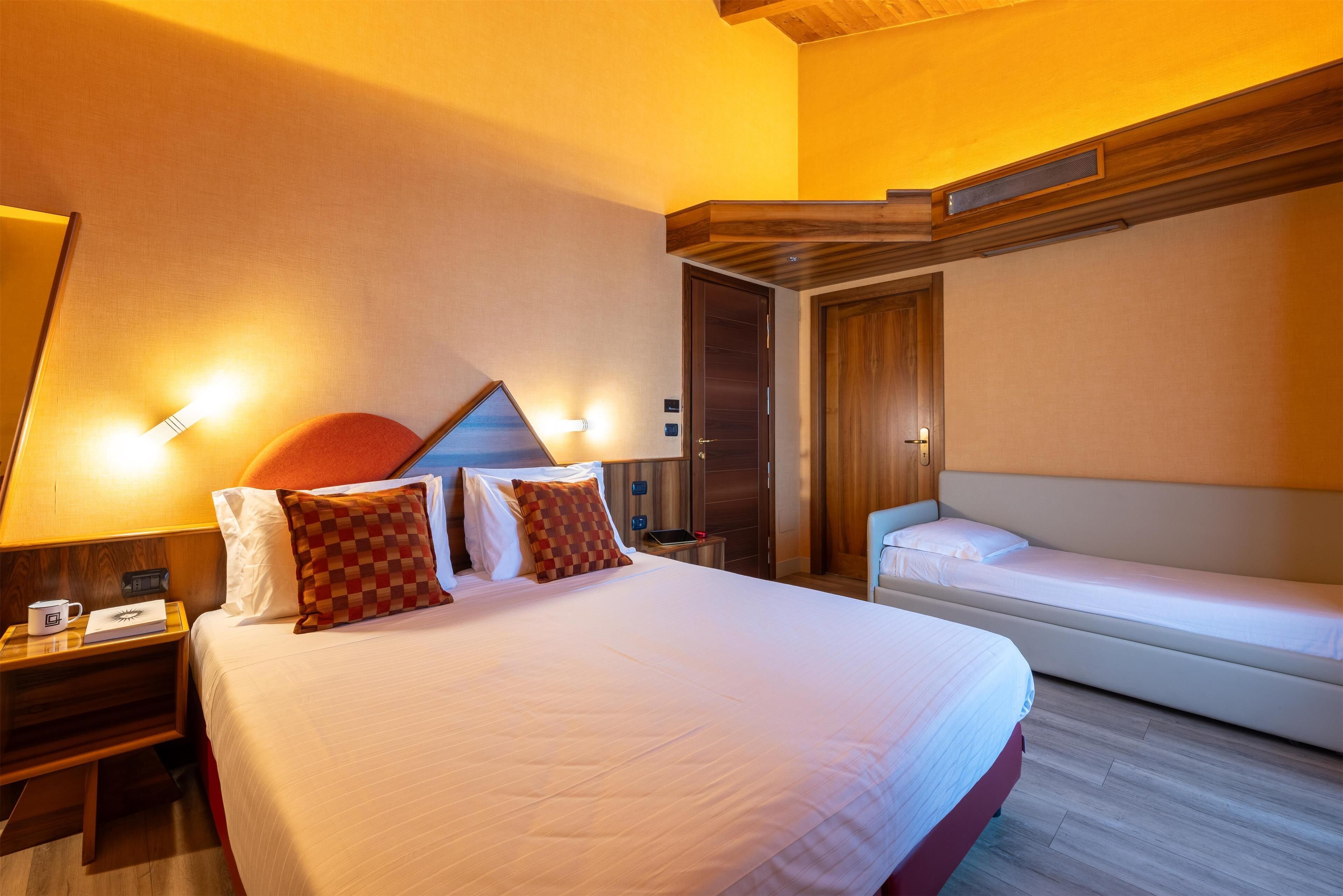 A hotel room with a large bed, bedside tables, a desk, and a built-in bench.