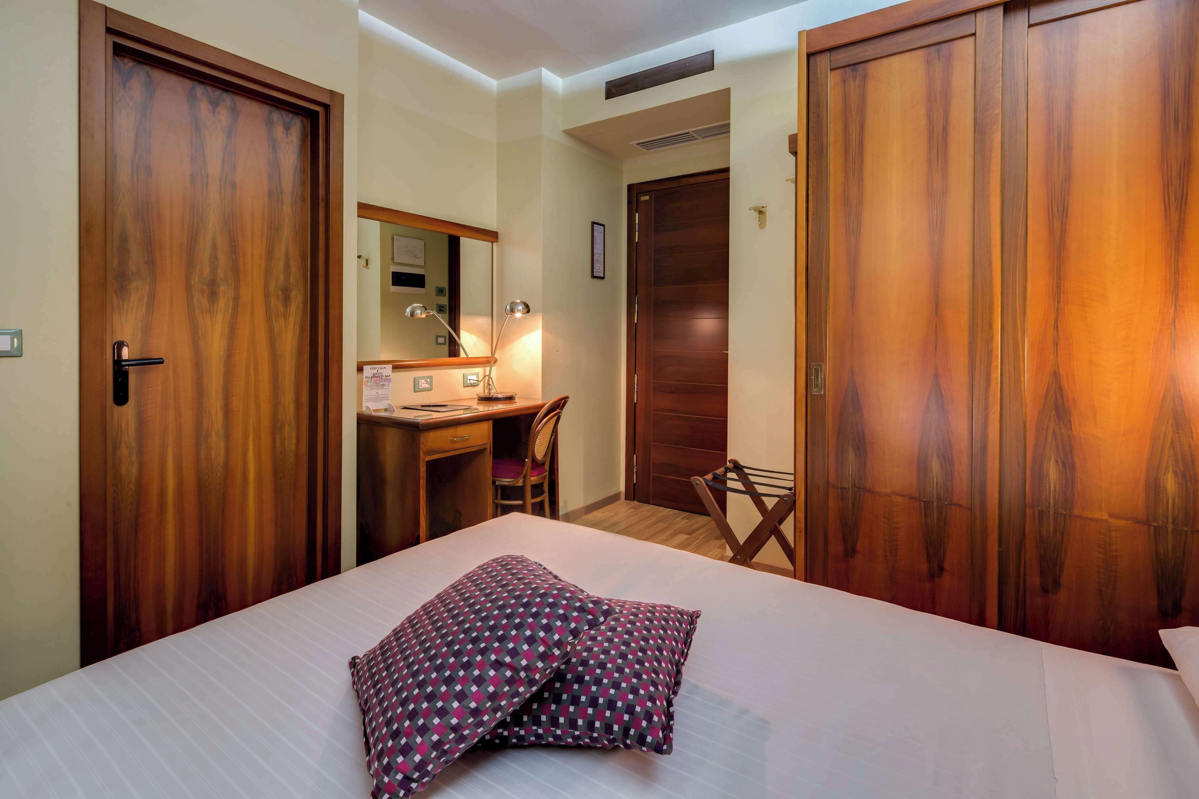 Habitación de hotel con cama, escritorio, silla, espejo y puertas de madera.