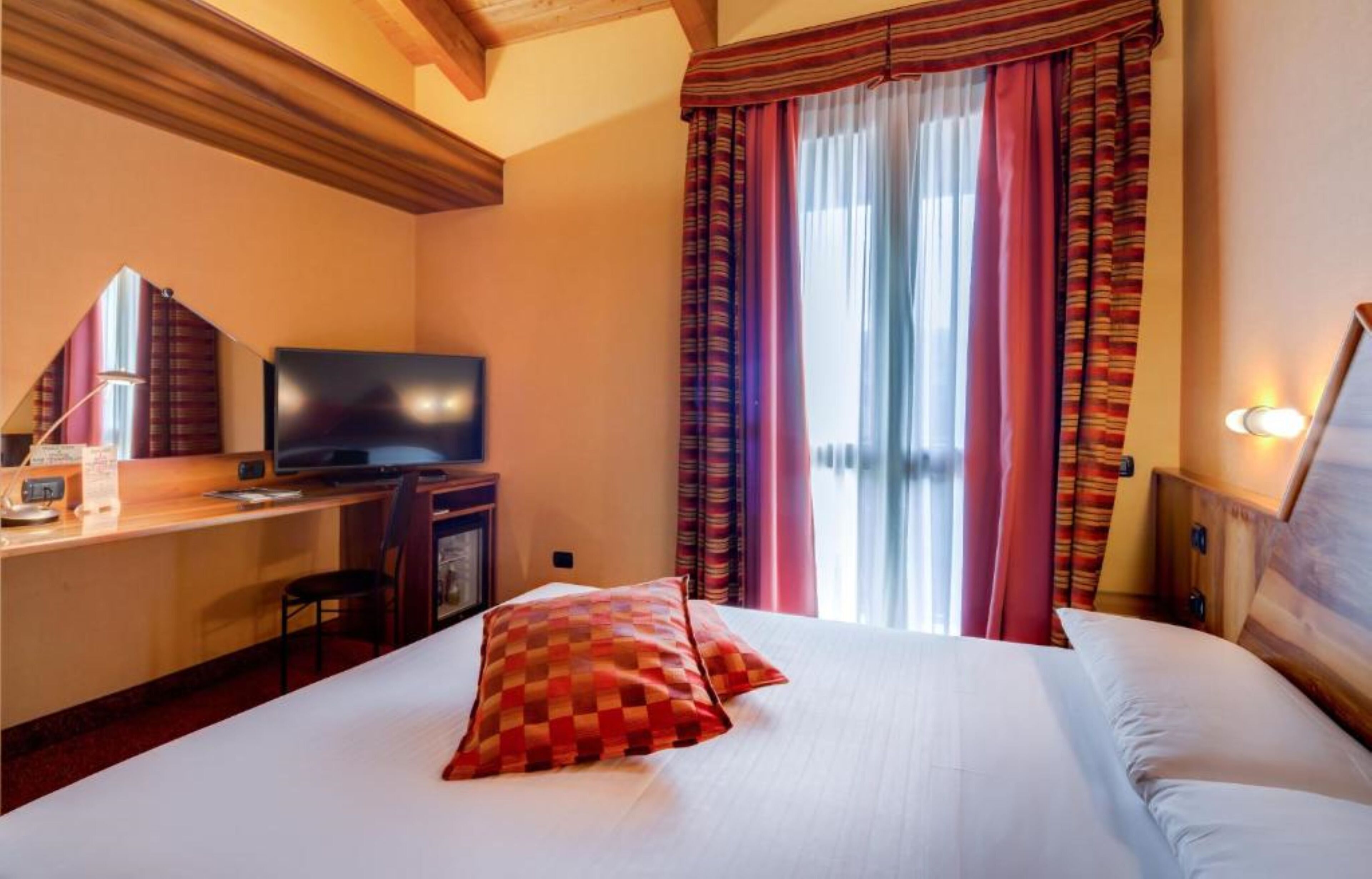 A hotel room with a bed, a desk with a computer, a television, and a window with curtains.