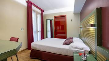 A hotel room with a bed, a desk, a chair, a nightstand, and a window with curtains.