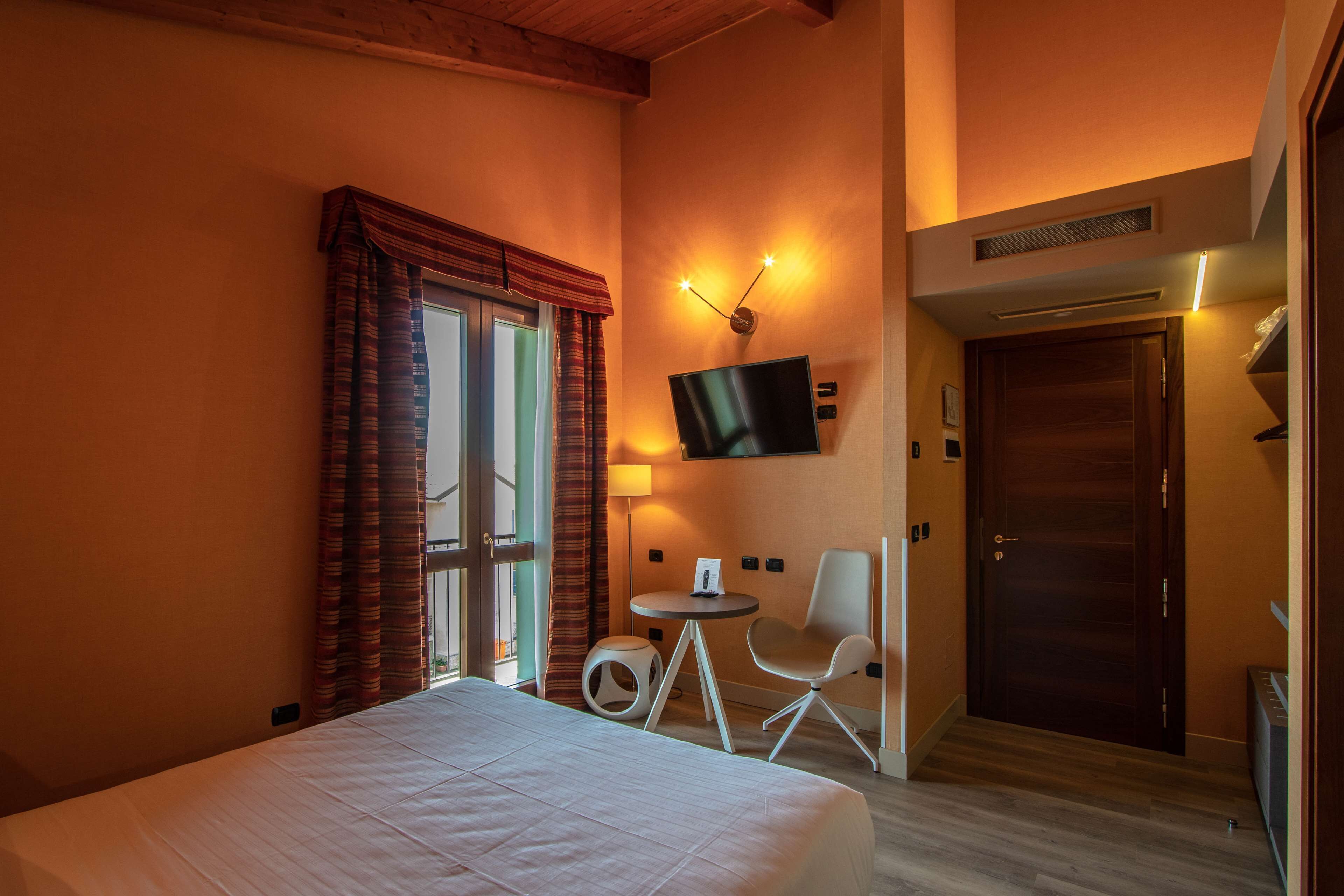 Une chambre d’hôtel avec un lit, un téléviseur fixé au mur, une petite table, une chaise et une porte.