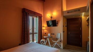 Une chambre d’hôtel avec un lit, un téléviseur fixé au mur, une petite table, une chaise et une porte.
