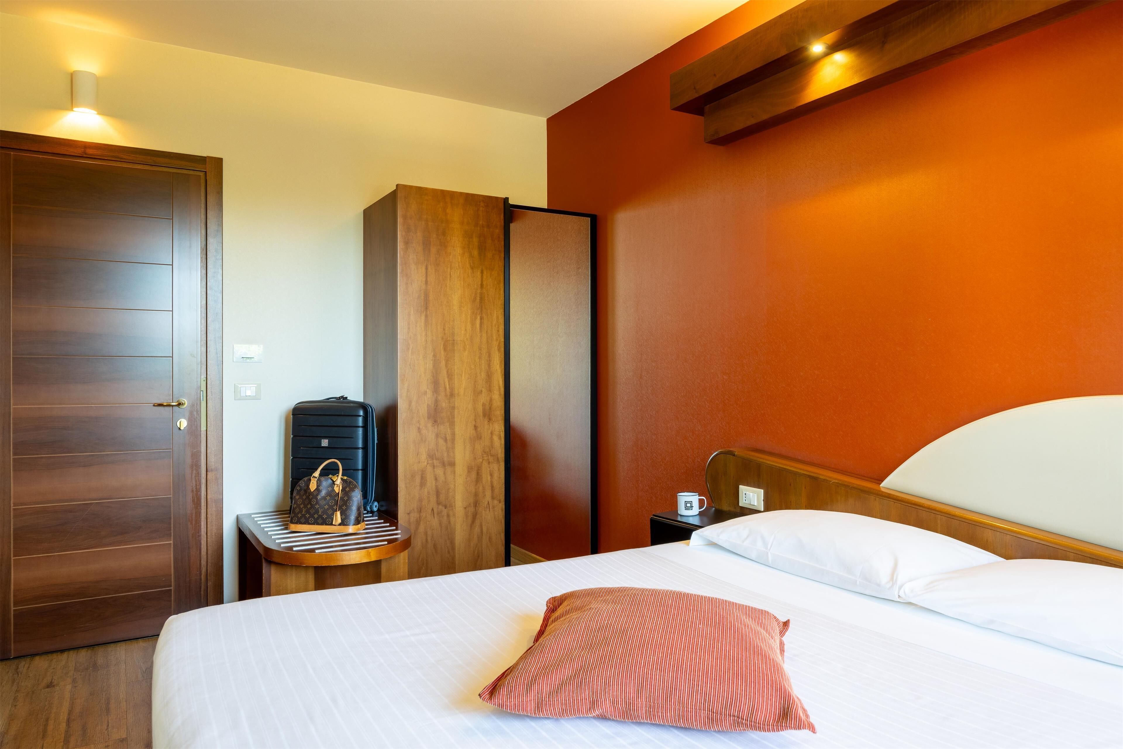 Una habitación de hotel con una cama, una mesita de noche, una maleta y un armario.